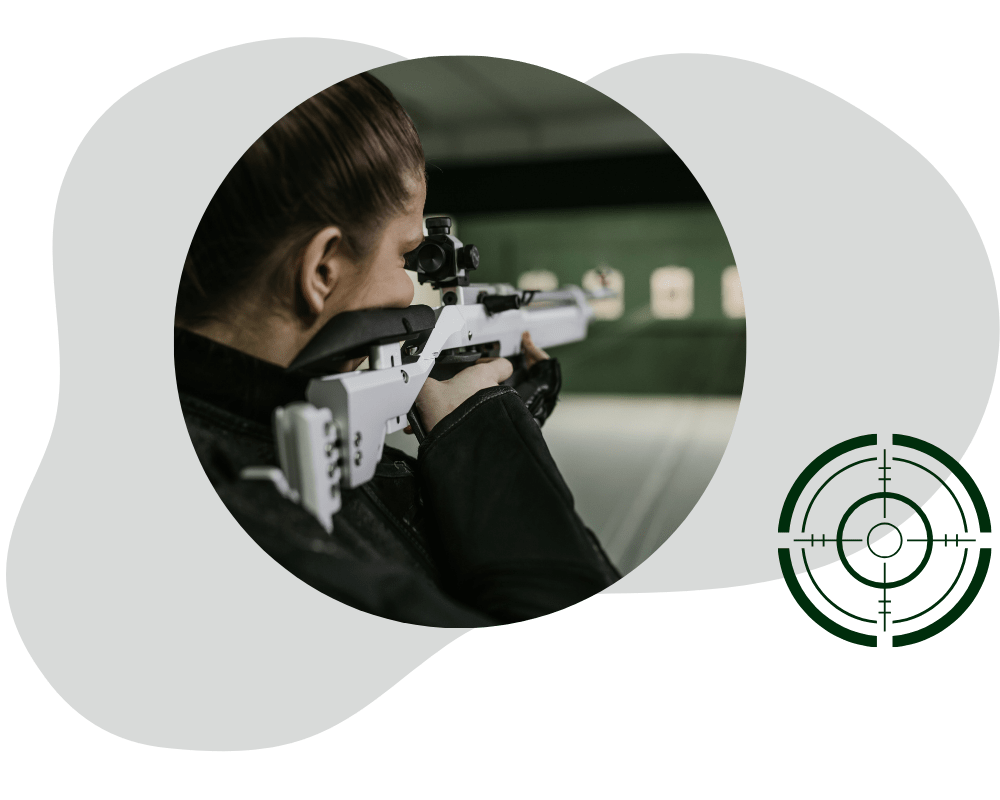 Header Schützenverein Apen Frau zielt mit einem modernen Luftgewehr auf eine Schießscheibe in einer Schießhalle. Im Vordergrund ist ein stilisiertes Fadenkreuz-Logo zu sehen.
